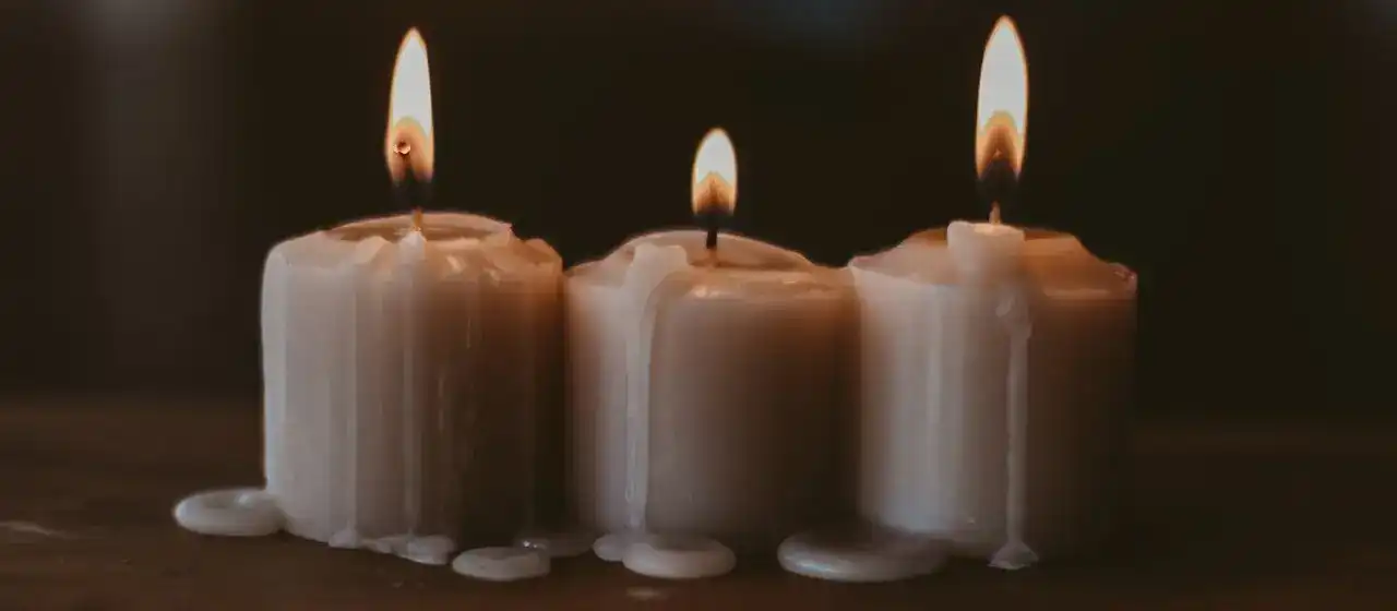 Three white candles standing in a row, burning on a wooden table.