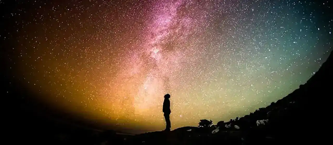 A silhouette of a man gazing upwards at a vibrant, star-filled sky.